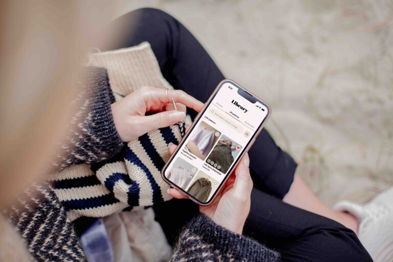 A woman is knitting while browsing the Knit&Note-app.