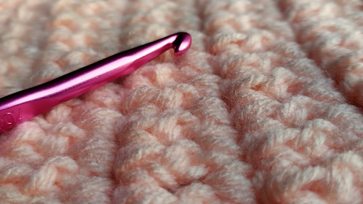 Close up of hot pink tapered crochet hook and crochet yarn in peach colour